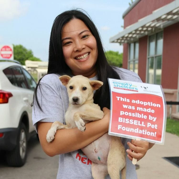Woman holding a small tan puppy she adopted during Empty the Shelters