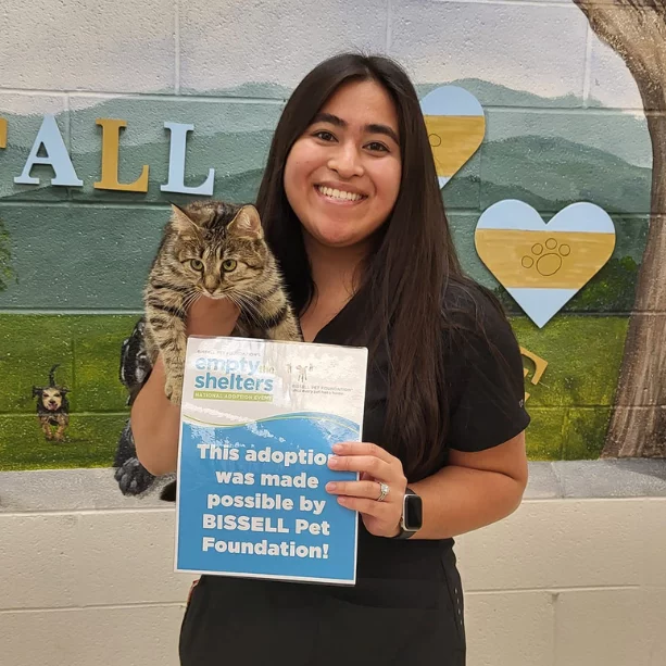 Woman holding tabby cat and adoption sign