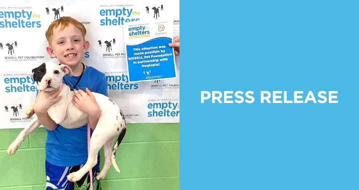 Young boy holds a puppy in front of a Empty the Shelters backdrop celebrating the adoption.