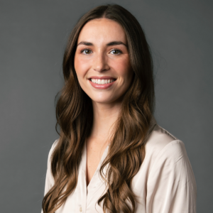 A young woman with long brown hair and a light beige blouse smiles at the camera against a plain gray background.