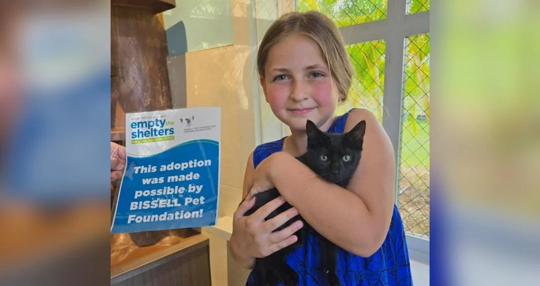 A young girl holding a black kitten and a sign that reads, This adoption was made possible by BISSELL Pet Foundation.